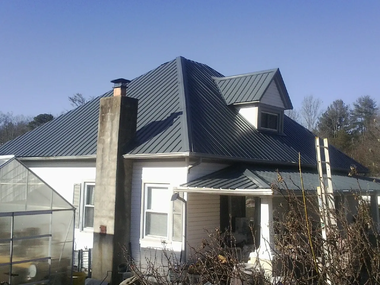 Dark blue standing seam metal roof on a white farmhouse with dormer — Slate & Tile Roof Repair by Roofing Brothers in New Johnsonville