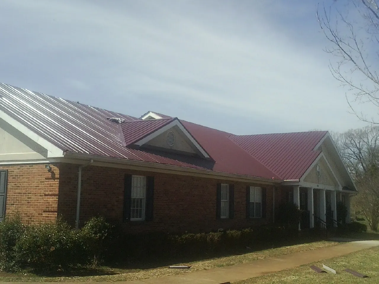 Red metal roof with gabled entries on a long brick building, from a Hail Damage Roof Repair job in New Johnsonville