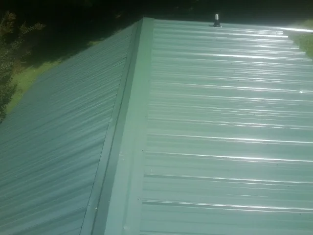 New green metal panels meeting at the ridge of a roof — Flat Roof Repair work by our crew in New Johnsonville
