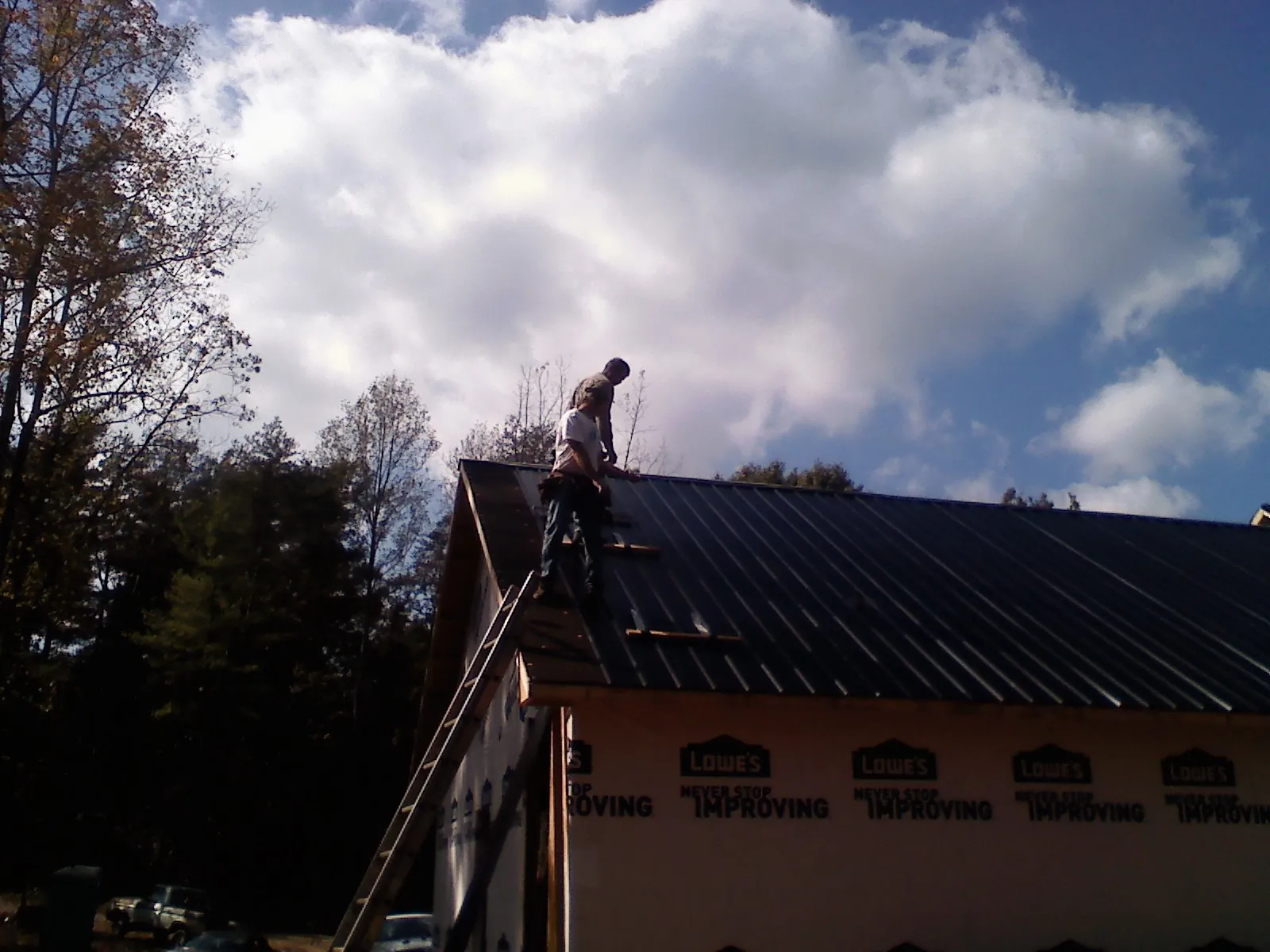 Roofer fastening dark metal panels high against a cloudy sky, from a Roof Inspection job in New Johnsonville