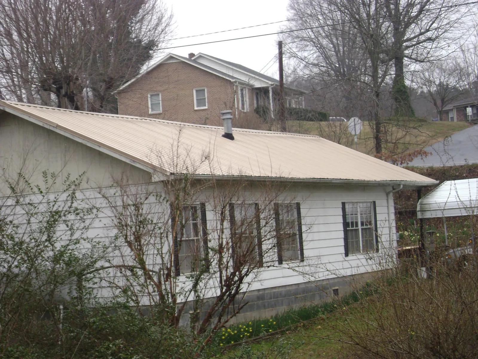 Tan metal roof on a white sided house set into a hillside — Commercial Roofing by Roofing Brothers in New Johnsonville